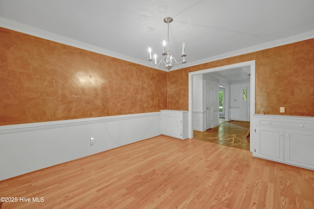 spare room with a chandelier, wainscoting, light wood finished floors, crown molding, and a decorative wall