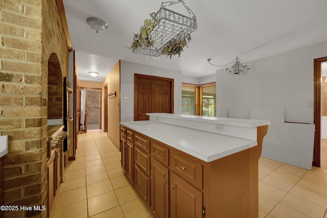kitchen featuring light tile patterned flooring, light countertops, brick wall, a kitchen island, and a chandelier
