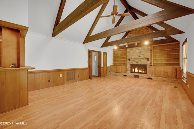 unfurnished living room featuring high vaulted ceiling, beamed ceiling, built in shelves, wainscoting, and wood finished floors