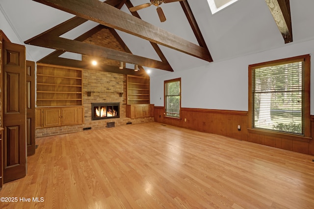unfurnished living room featuring a wainscoted wall, beam ceiling, light wood-type flooring, built in shelves, and a fireplace
