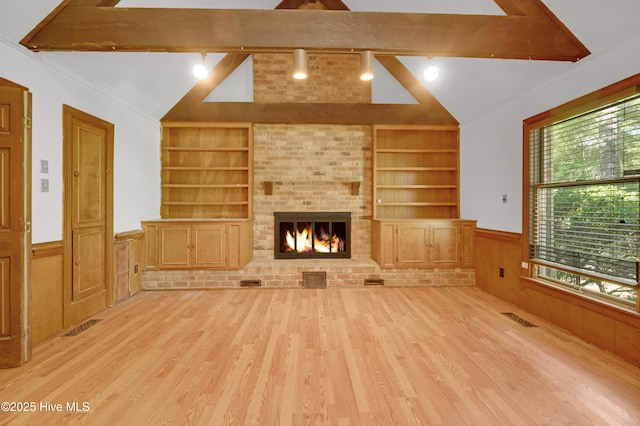 unfurnished living room with built in shelves, wainscoting, rail lighting, wood finished floors, and a brick fireplace