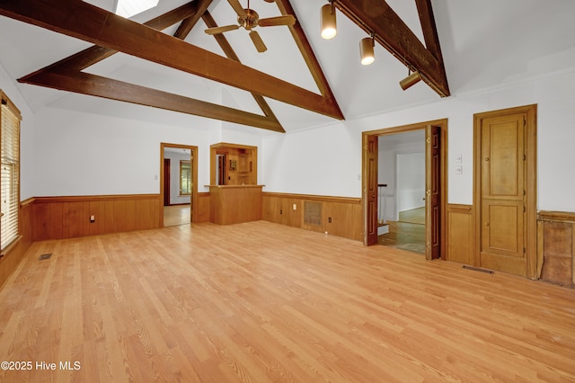 unfurnished living room with a wainscoted wall, beam ceiling, wood finished floors, high vaulted ceiling, and a ceiling fan