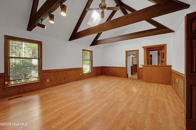 unfurnished living room featuring wainscoting, light wood-type flooring, rail lighting, wooden walls, and ceiling fan