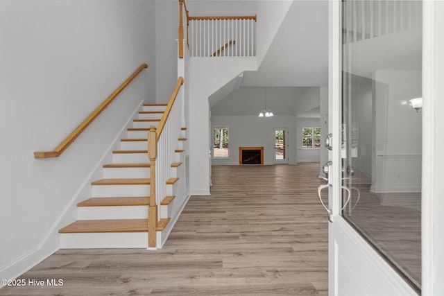 staircase featuring a towering ceiling, wood finished floors, a fireplace, and baseboards