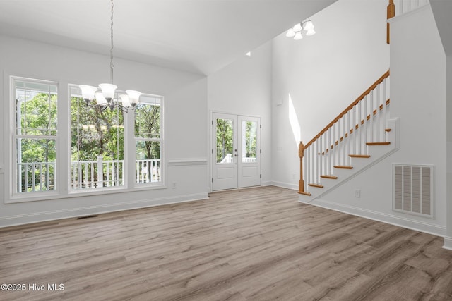 unfurnished living room with a chandelier, stairway, wood finished floors, baseboards, and a high ceiling