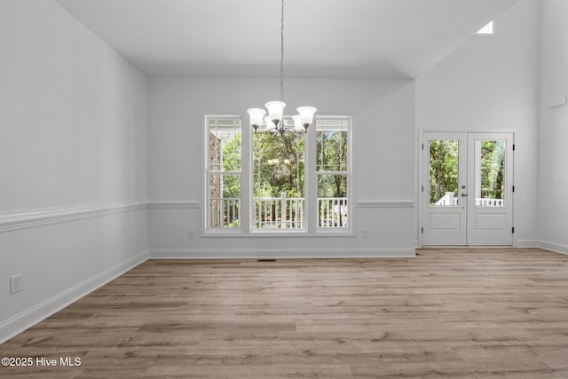 unfurnished dining area with a chandelier, wood finished floors, baseboards, and french doors