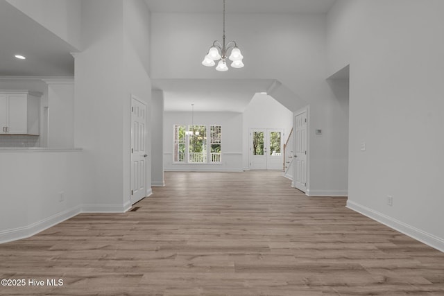unfurnished dining area with a chandelier, light wood-type flooring, a high ceiling, baseboards, and recessed lighting