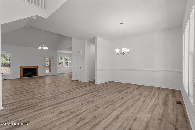 unfurnished living room featuring a chandelier, wood finished floors, high vaulted ceiling, a fireplace, and baseboards