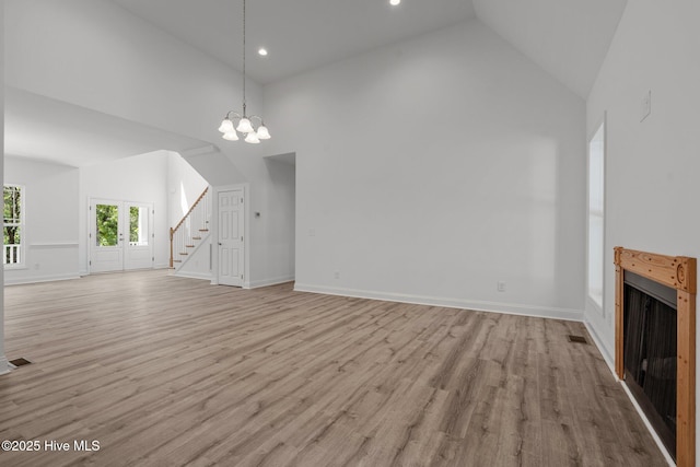 unfurnished living room with high vaulted ceiling, stairs, light wood-type flooring, a chandelier, and baseboards