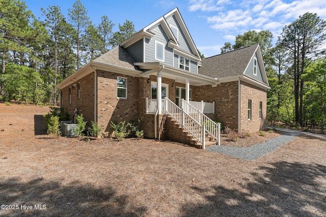 view of front of property featuring brick siding, a porch, roof with shingles, stairs, and cooling unit
