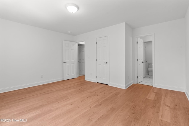 unfurnished bedroom featuring baseboards, light wood finished floors, and ensuite bathroom