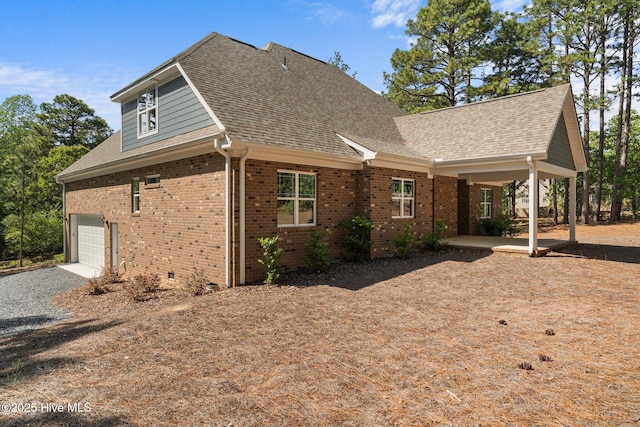 view of side of property with brick siding, gravel driveway, a garage, and roof with shingles