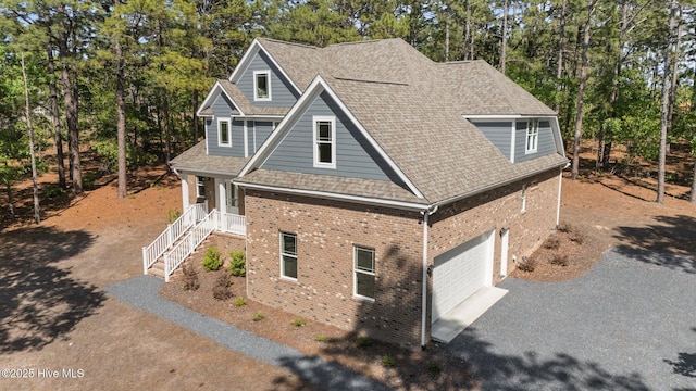 view of side of home with brick siding, asphalt driveway, view of scattered trees, and a porch
