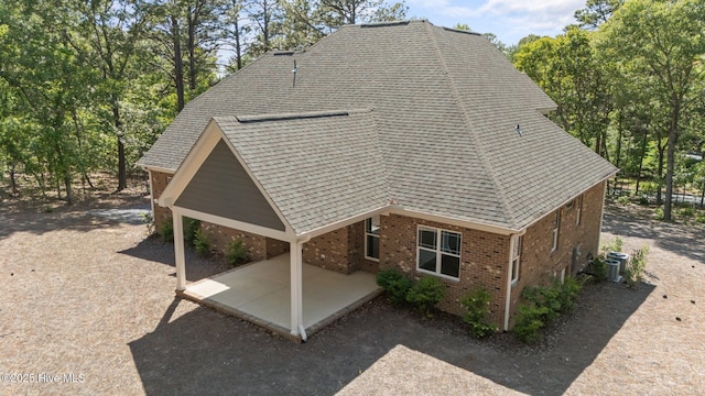 view of property exterior with a patio, brick siding, central AC unit, and a shingled roof