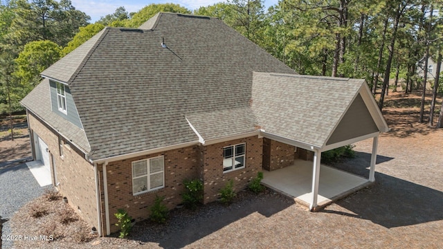 view of home's exterior featuring brick siding, a shingled roof, a patio, and view of scattered trees