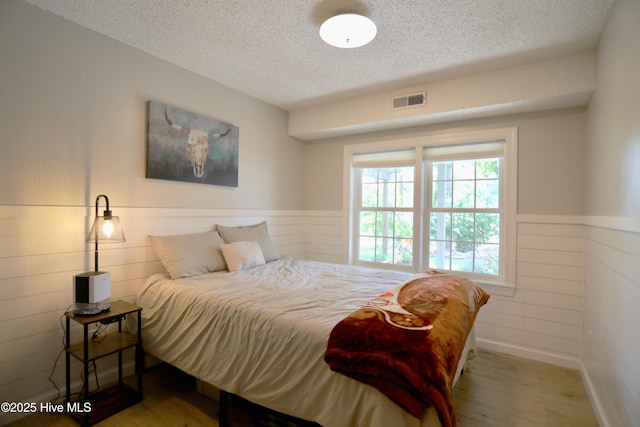 bedroom featuring a textured ceiling, wood finished floors, and a wainscoted wall