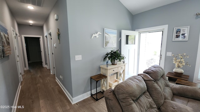 hallway featuring wood finished floors, baseboards, and vaulted ceiling