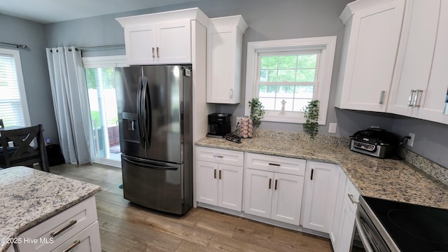 kitchen with black refrigerator with ice dispenser, light wood finished floors, white cabinetry, and light stone countertops