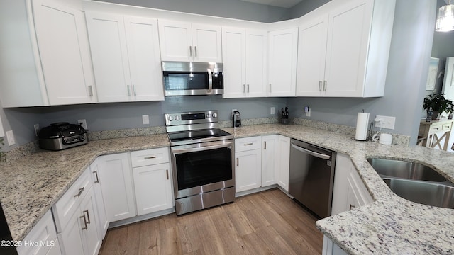 kitchen with stainless steel appliances, white cabinetry, light wood-style flooring, and light stone countertops