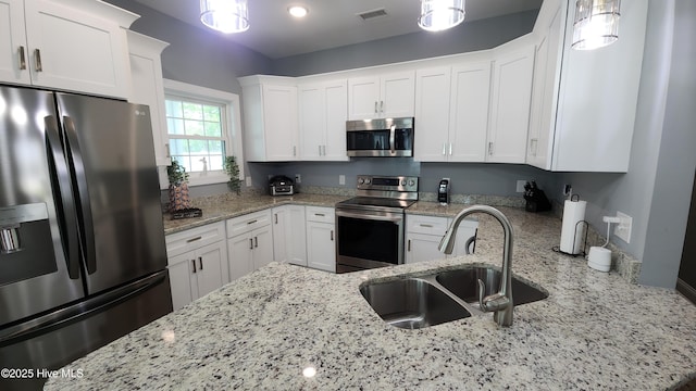 kitchen with stainless steel appliances, a sink, white cabinets, light stone countertops, and hanging light fixtures