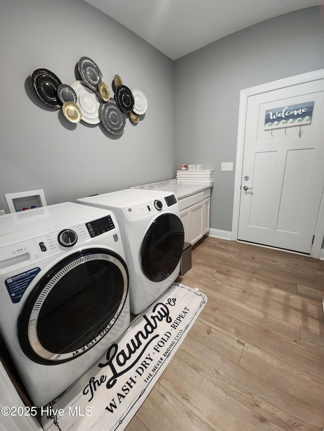 clothes washing area with washer and dryer, cabinet space, and light wood-style flooring