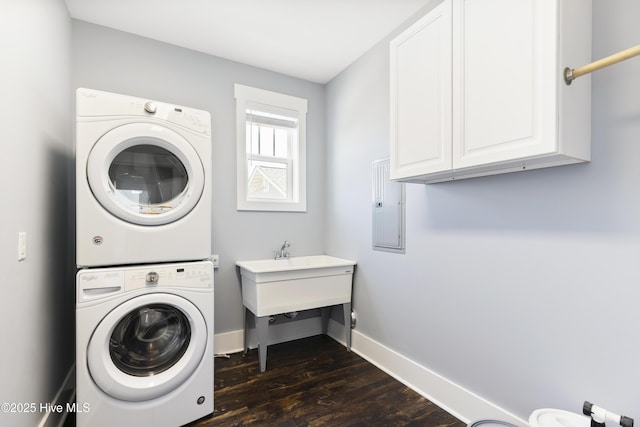 clothes washing area featuring estacked washer and dryer, cabinet space, dark wood-style floors, and baseboards