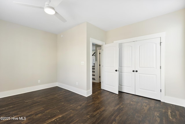 unfurnished bedroom with baseboards, dark wood finished floors, a closet, and a ceiling fan
