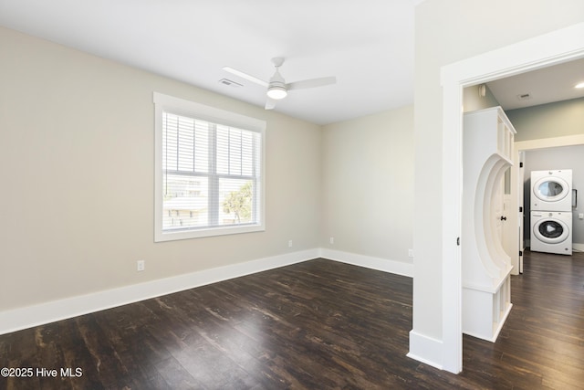 unfurnished room with estacked washer and dryer, a ceiling fan, dark wood-style floors, and baseboards