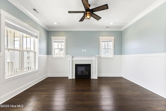 unfurnished living room with a wainscoted wall, plenty of natural light, ceiling fan, a glass covered fireplace, and dark wood-type flooring