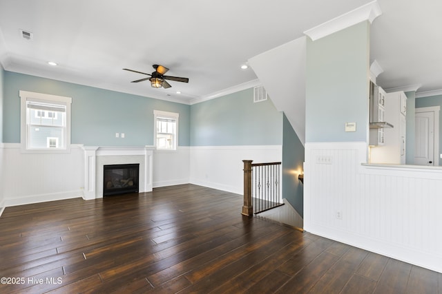 unfurnished living room featuring wainscoting, ceiling fan, wood-type flooring, a glass covered fireplace, and ornamental molding