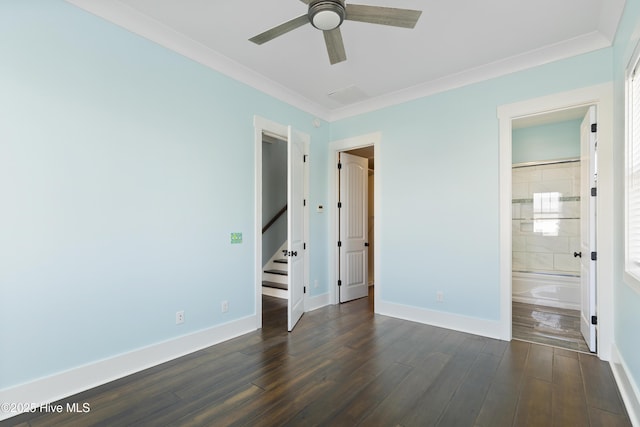 unfurnished bedroom featuring baseboards, crown molding, dark wood-type flooring, ensuite bathroom, and a ceiling fan