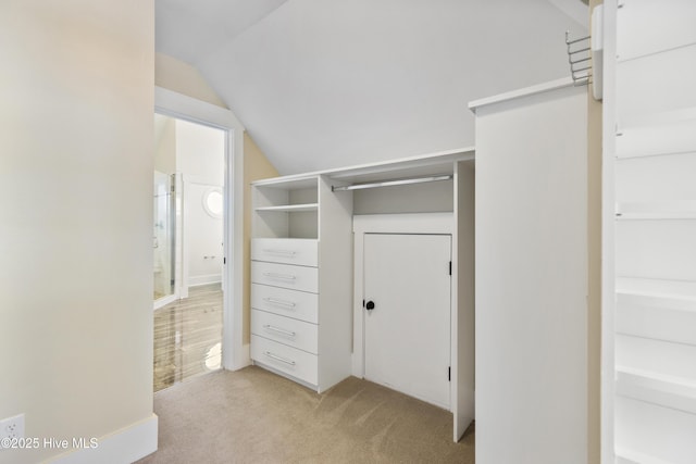walk in closet with light carpet and vaulted ceiling