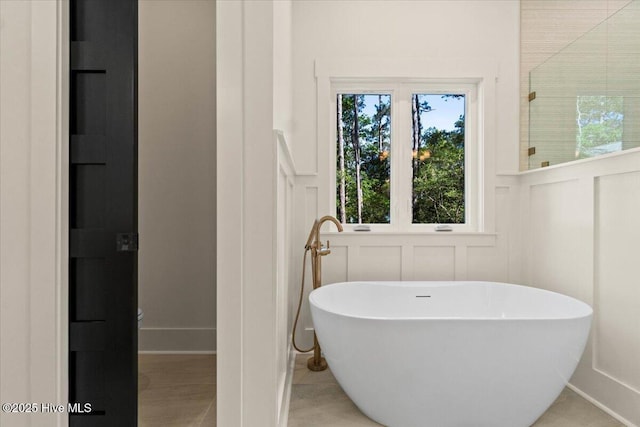 full bathroom featuring a decorative wall, a freestanding bath, and a wainscoted wall