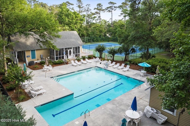 community pool with a patio, fence, an outbuilding, and view of wooded area