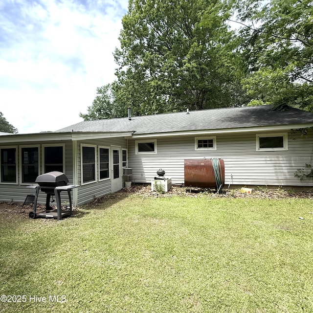 rear view of house featuring heating fuel, a lawn, and roof with shingles