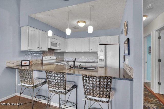1912 Goose Creek Rd SW Unit 4302, Ocean Isle Beach, NC 28469 - kitchen with white appliances, a peninsula, dark wood-style flooring, white cabinets, and dark countertops
