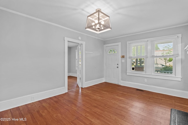 foyer entrance featuring a chandelier, ornamental molding, baseboards, and wood finished floors