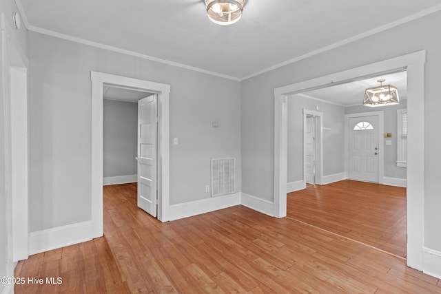 unfurnished room with ornamental molding, a chandelier, light wood-type flooring, and baseboards