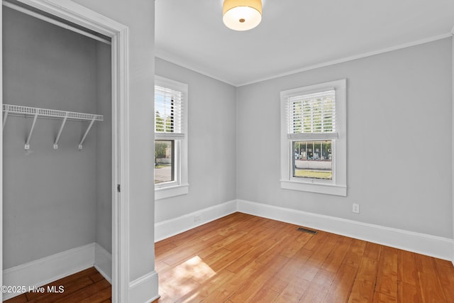 unfurnished bedroom with multiple windows, crown molding, hardwood / wood-style flooring, and baseboards