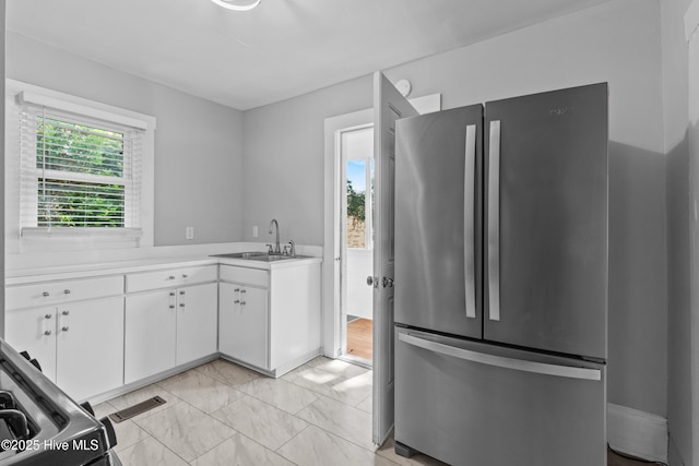 kitchen with freestanding refrigerator, a sink, light countertops, white cabinets, and light marble finish floors