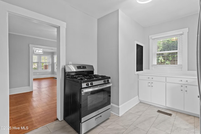 kitchen featuring stainless steel gas stove, baseboards, plenty of natural light, and white cabinetry