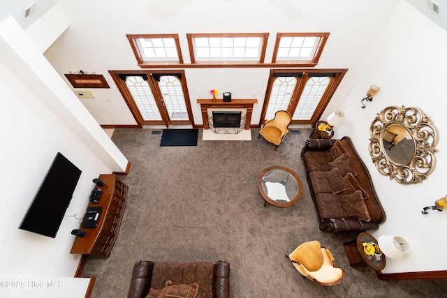 carpeted living area with french doors, a fireplace with flush hearth, a towering ceiling, and baseboards