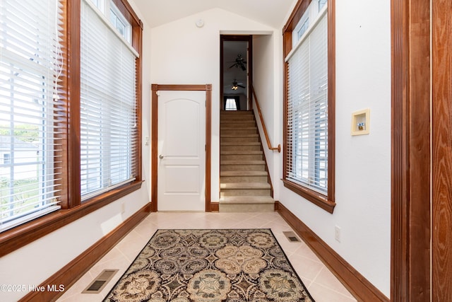 foyer featuring light tile patterned floors, plenty of natural light, lofted ceiling, baseboards, and stairway