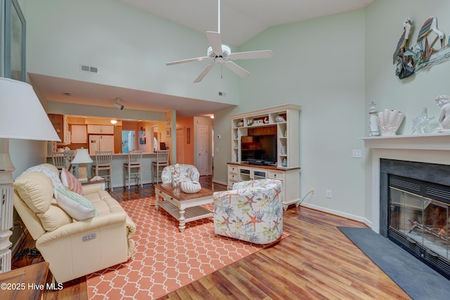 6025 Inland Greens Dr, Wilmington, NC 28405 - living room featuring wood finished floors, a fireplace with flush hearth, a ceiling fan, high vaulted ceiling, and baseboards