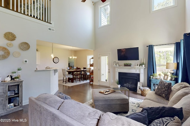 living room with a towering ceiling, healthy amount of natural light, dark wood-type flooring, and a glass covered fireplace