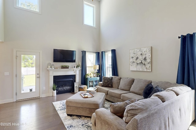 living area with a high ceiling, wood finished floors, a glass covered fireplace, and baseboards