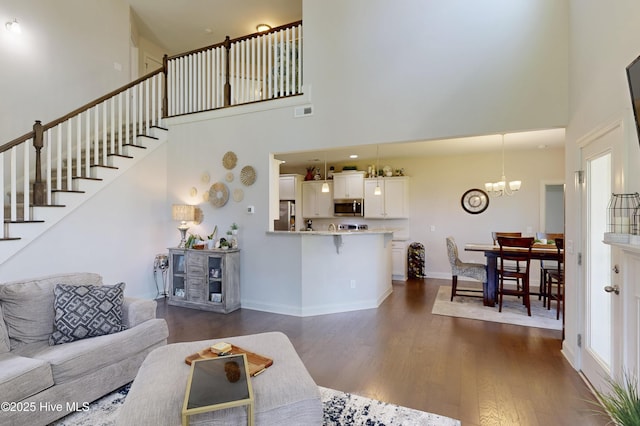 living room with a towering ceiling, a chandelier, dark wood-style flooring, stairway, and baseboards