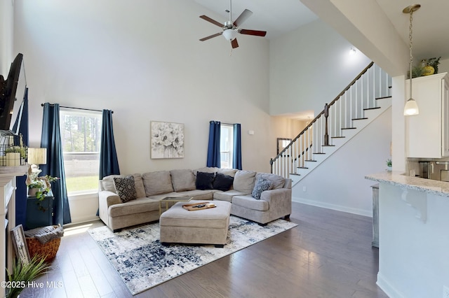 living room featuring a high ceiling, stairway, dark wood-style flooring, ceiling fan, and baseboards