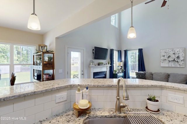 kitchen featuring open floor plan, plenty of natural light, a sink, light stone counters, and a high ceiling