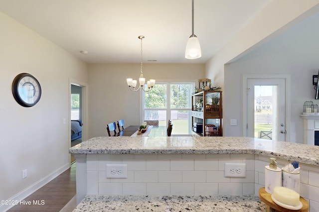 kitchen with a chandelier, dark wood finished floors, light stone counters, baseboards, and hanging light fixtures